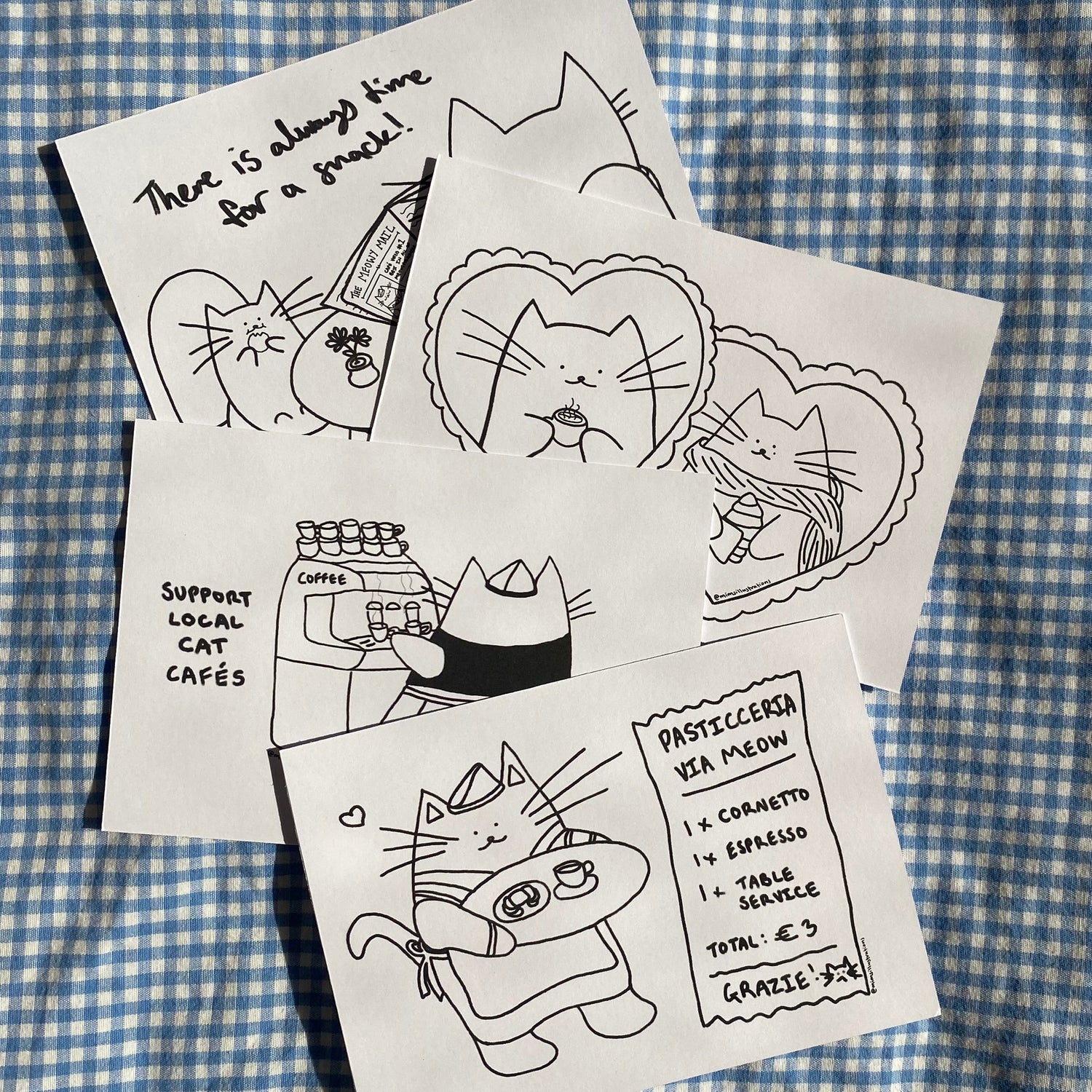 Set of four cat-themed cards on a blue and white checkered fabric background